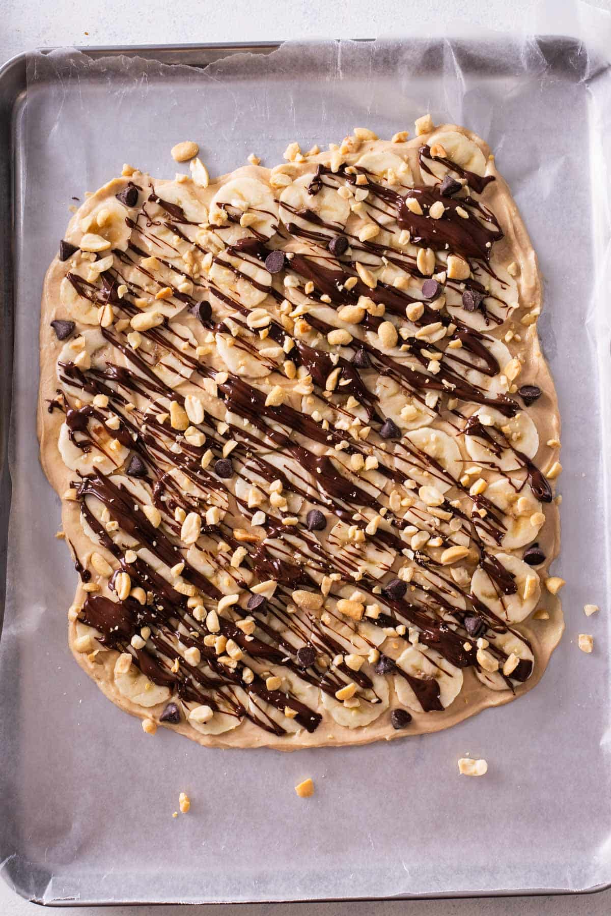 Chunky monkey frozen yogurt bark is topped with bananas, chocolate, and peanuts.