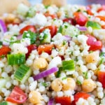 A big glass bowl full of a Mediterranean Couscous Salad with tomatoes, feta, garbanzo beans, and cucumbers.