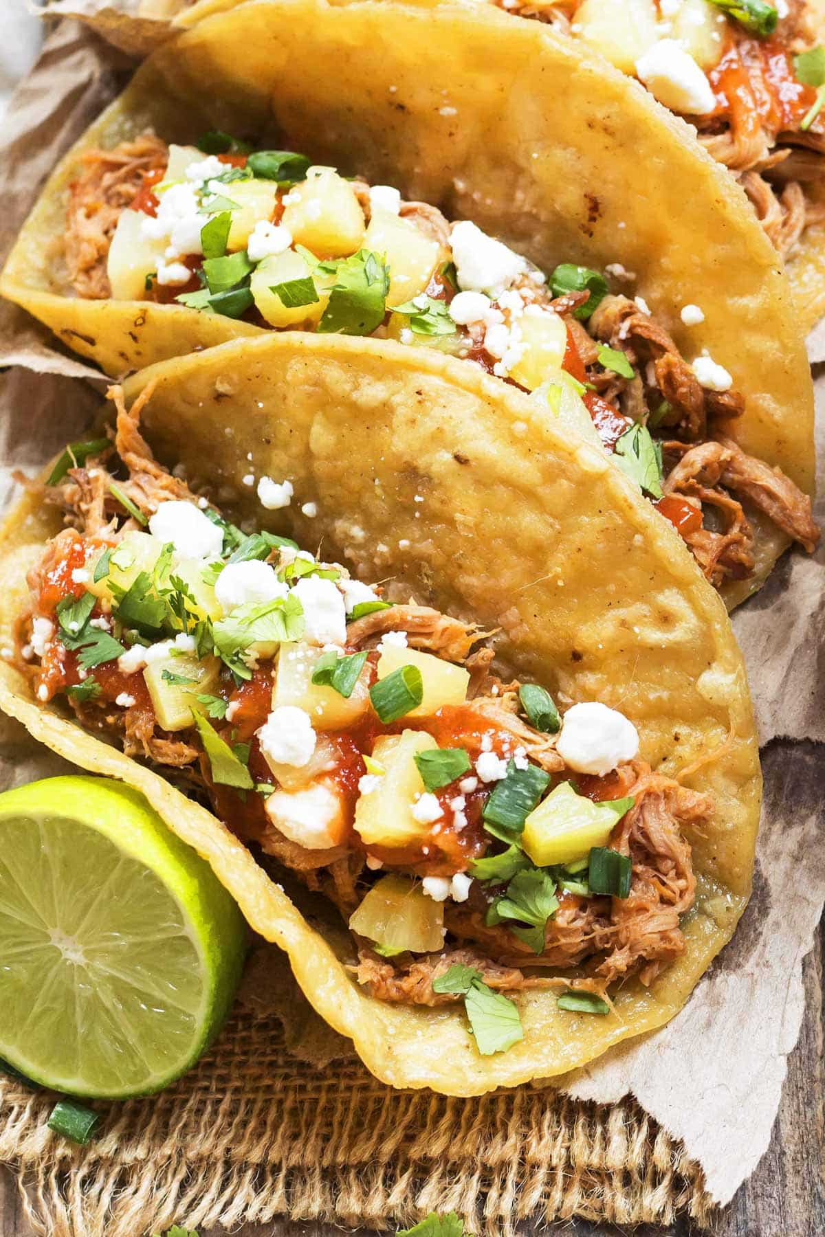 A row of Slow Cooker Pineapple Pulled Pork Tacos garnished with lime.