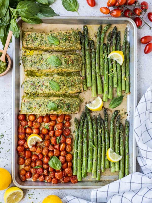Sheet Pan Salmon and Asparagus with pesto sauce and roasted cherry tomatoes is served with lemon wedges.