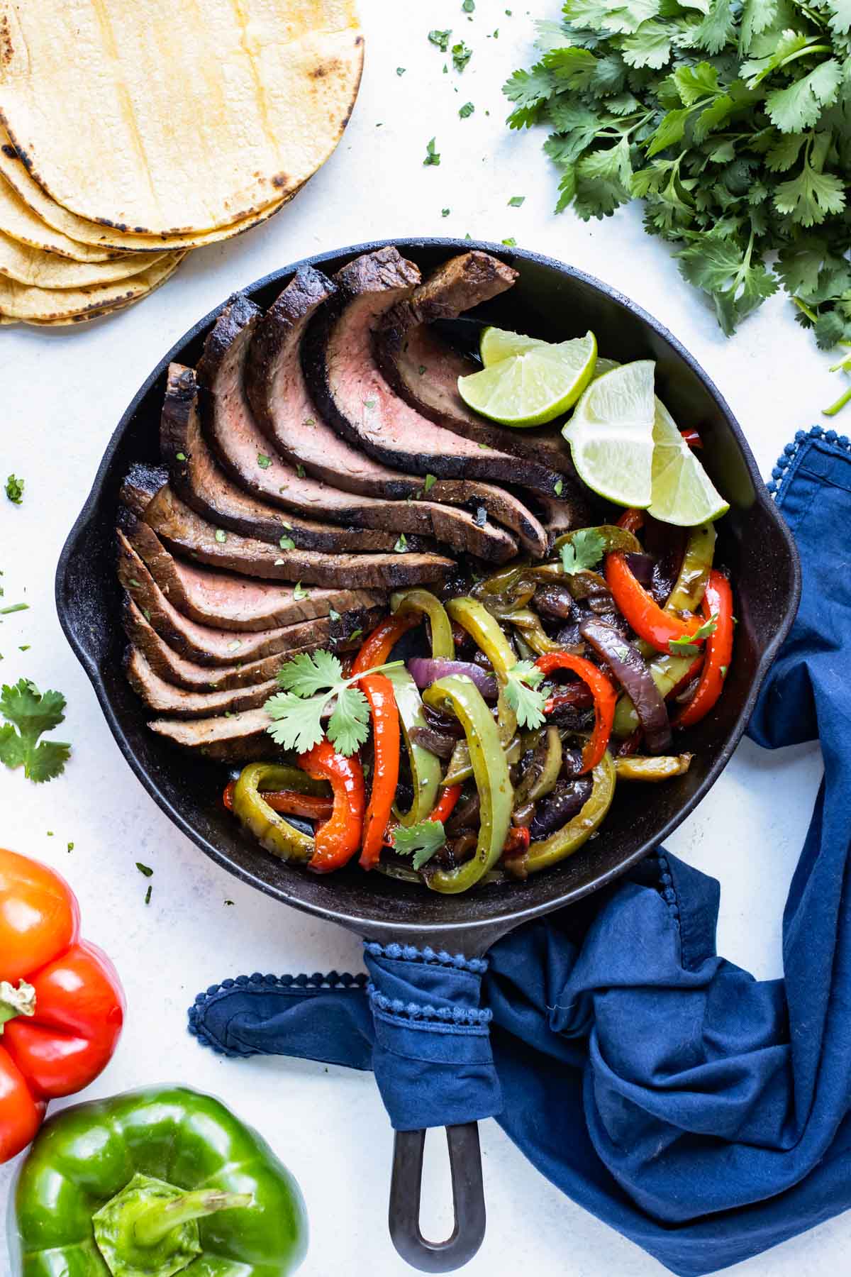 Best Flank Steak Fajitas RECIPE served in a cast iron skillet with limes and sauteed bell peppers.