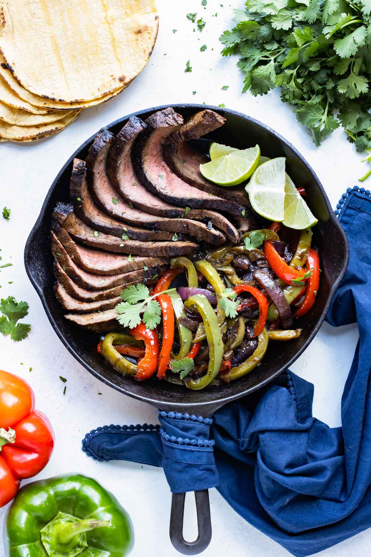 Sliced flank steak, fajita veggies, and limes served in a cast iron skillet.