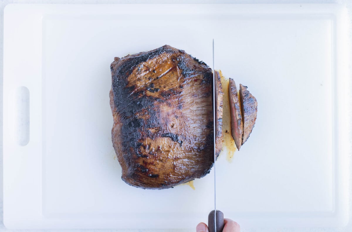 The cooked steak is sliced on top of a cutting board.