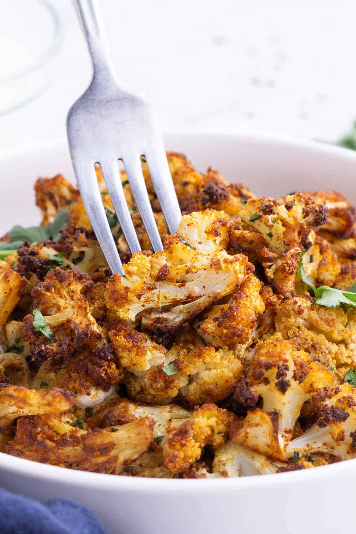 A fork picks up a piece of curry-roasted cauliflower.