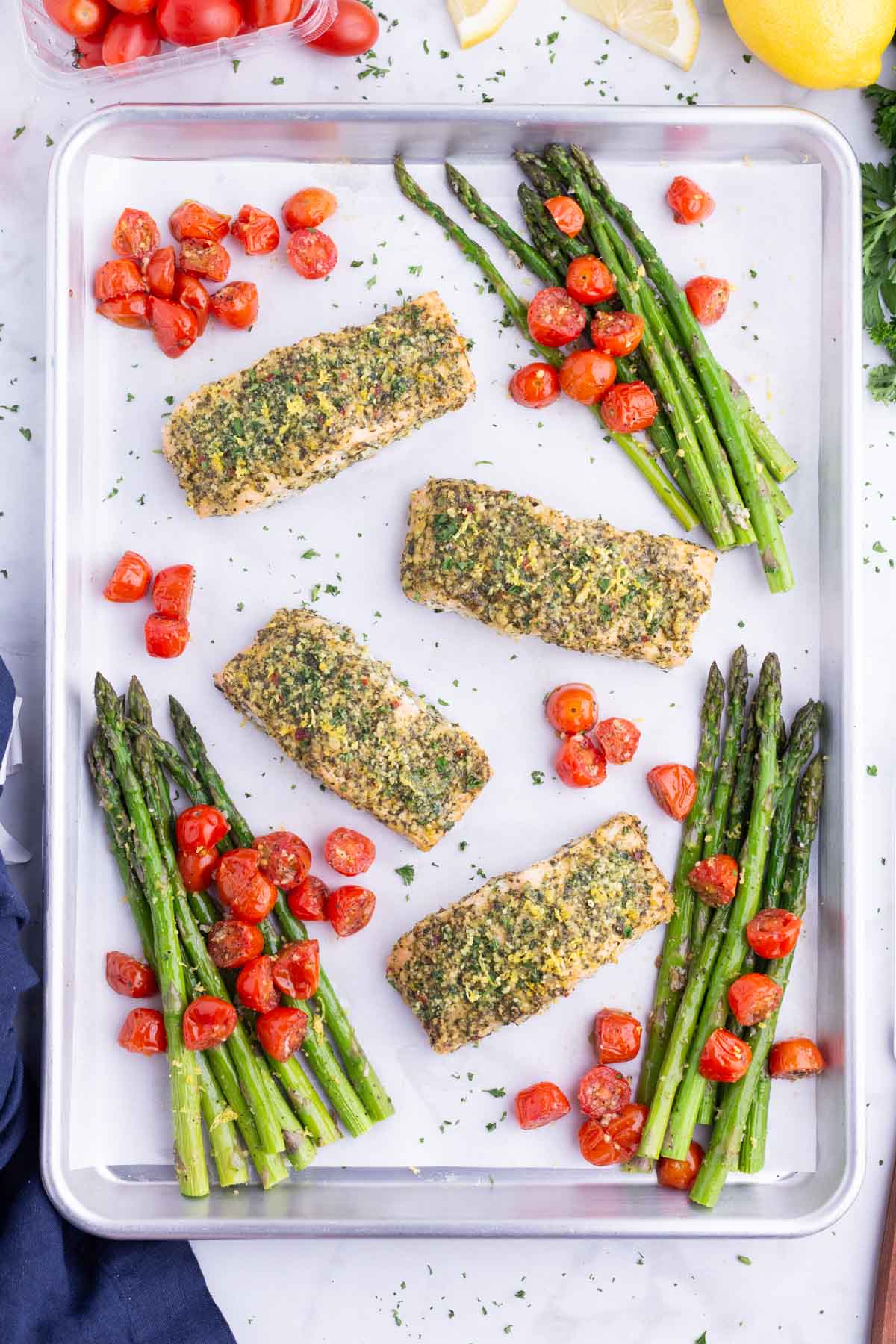 A baking sheet full of pesto salmon, roasted asparagus, and tomatoes.