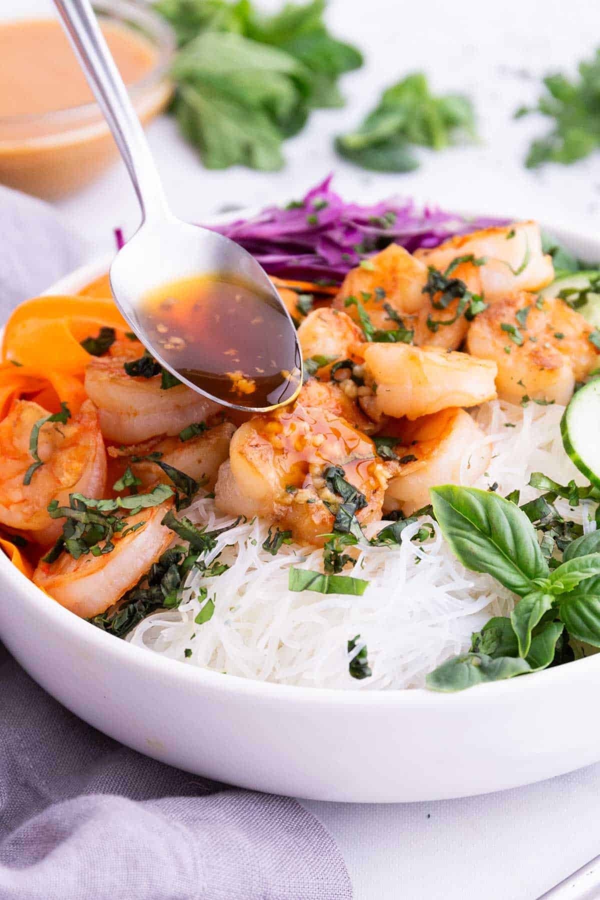 A spoon drizzles fish sauce over the rice in a bowl.