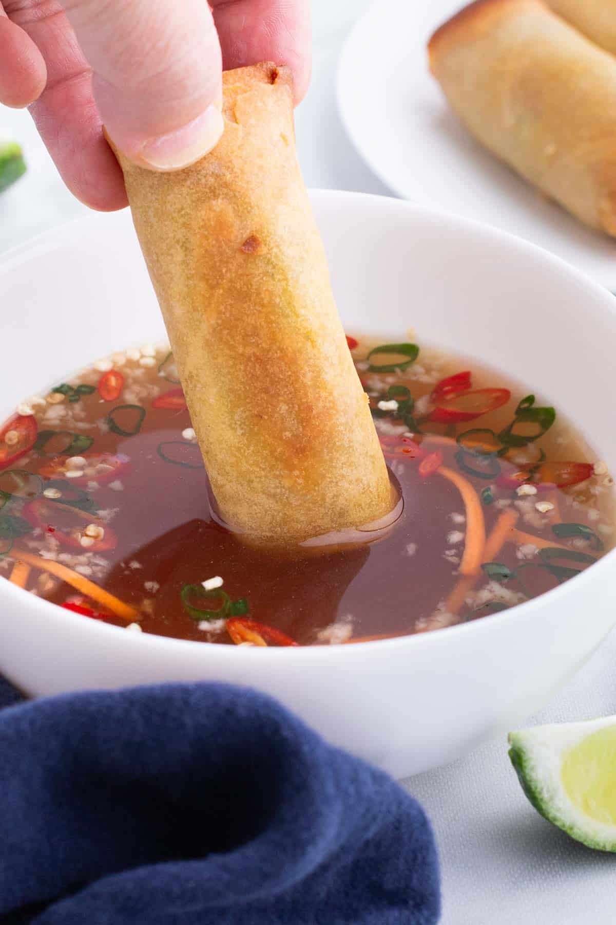 A spring roll is dipped into a bowl of fish sauce dipping sauce.