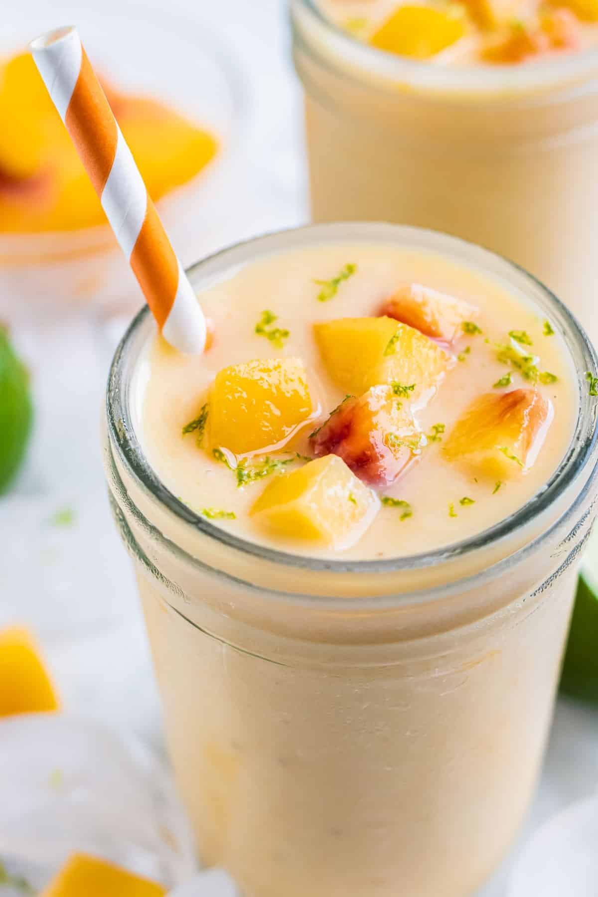 A frozen peach banana smoothie is served in a glass with a straw.