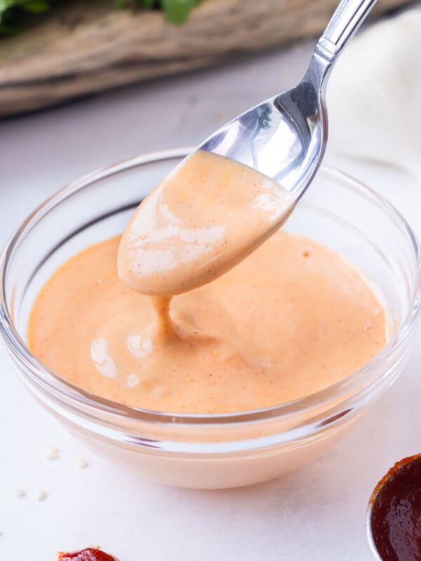 A spoon scoops up some spicy sriracha mayo sauce from a mixing bowl.