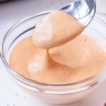 A spoon scoops up some homemade spicy sriracha mayo dipping sauce from a mixing bowl.