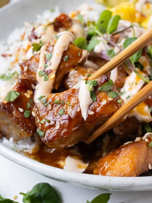 Chopsticks pick up a piece of crispy salmon from a rice bowl.