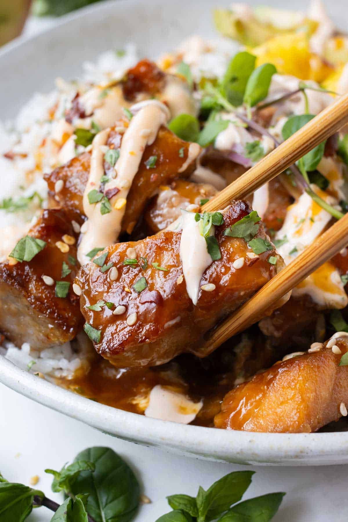 Chopsticks pick up a piece of crispy salmon from a rice bowl.