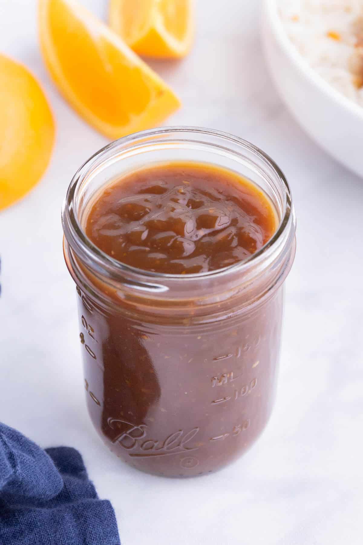 Homemade orange sauce is stored in a glass jar.
