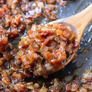 A wooden spoons scoops up some balsamic bacon onion jam from a skillet.
