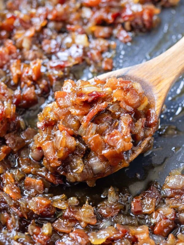 A wooden spoons scoops up some balsamic bacon onion jam from a skillet.
