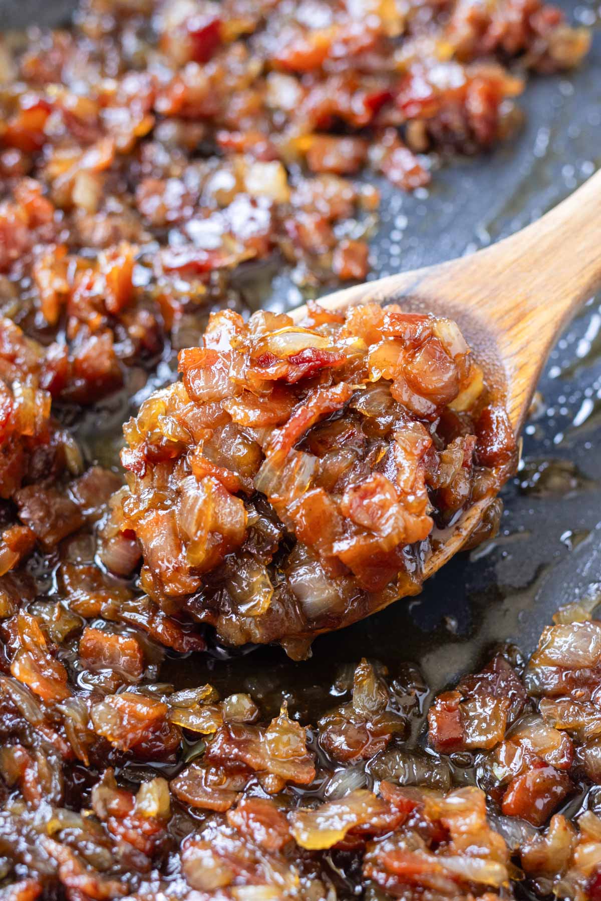 A wooden spoons scoops up some balsamic bacon onion jam from a skillet.