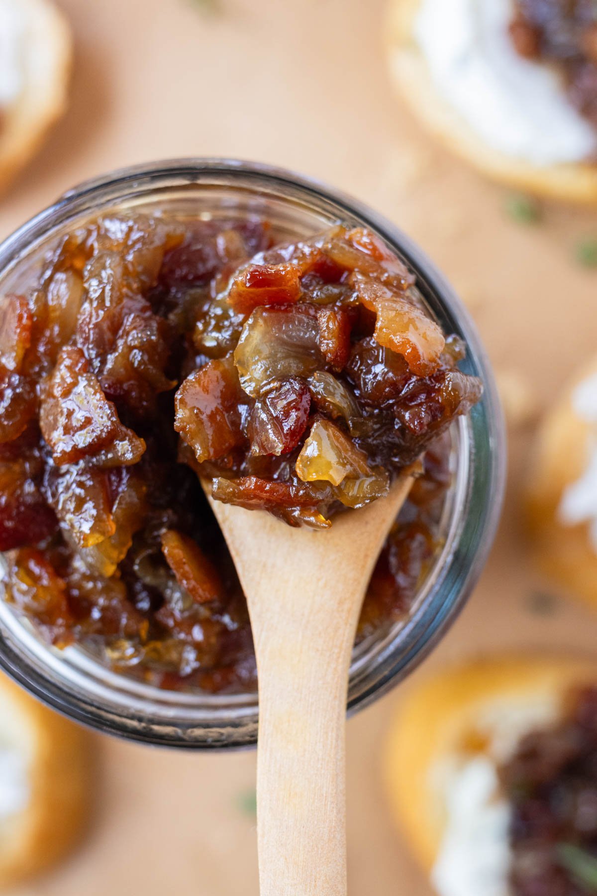 A spoon scoops up some  homemade Bacon Onion Jam from a glass jar.