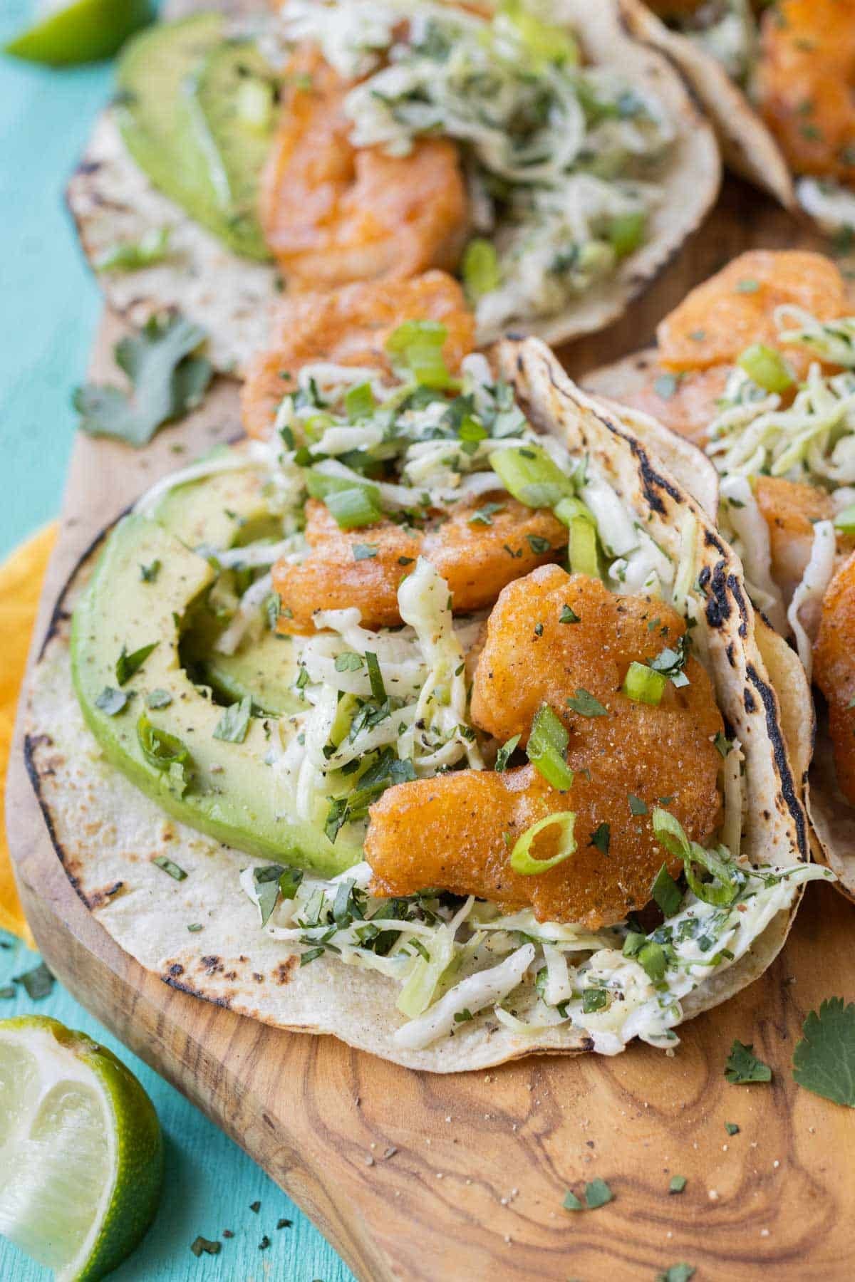 A plate full of beer-battered Baja shrimp tacos are served with a creamy slaw and avocado.
