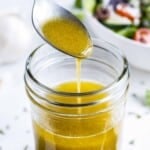 A spoon scoops up some homemade Greek salad dressing from a glass jar.