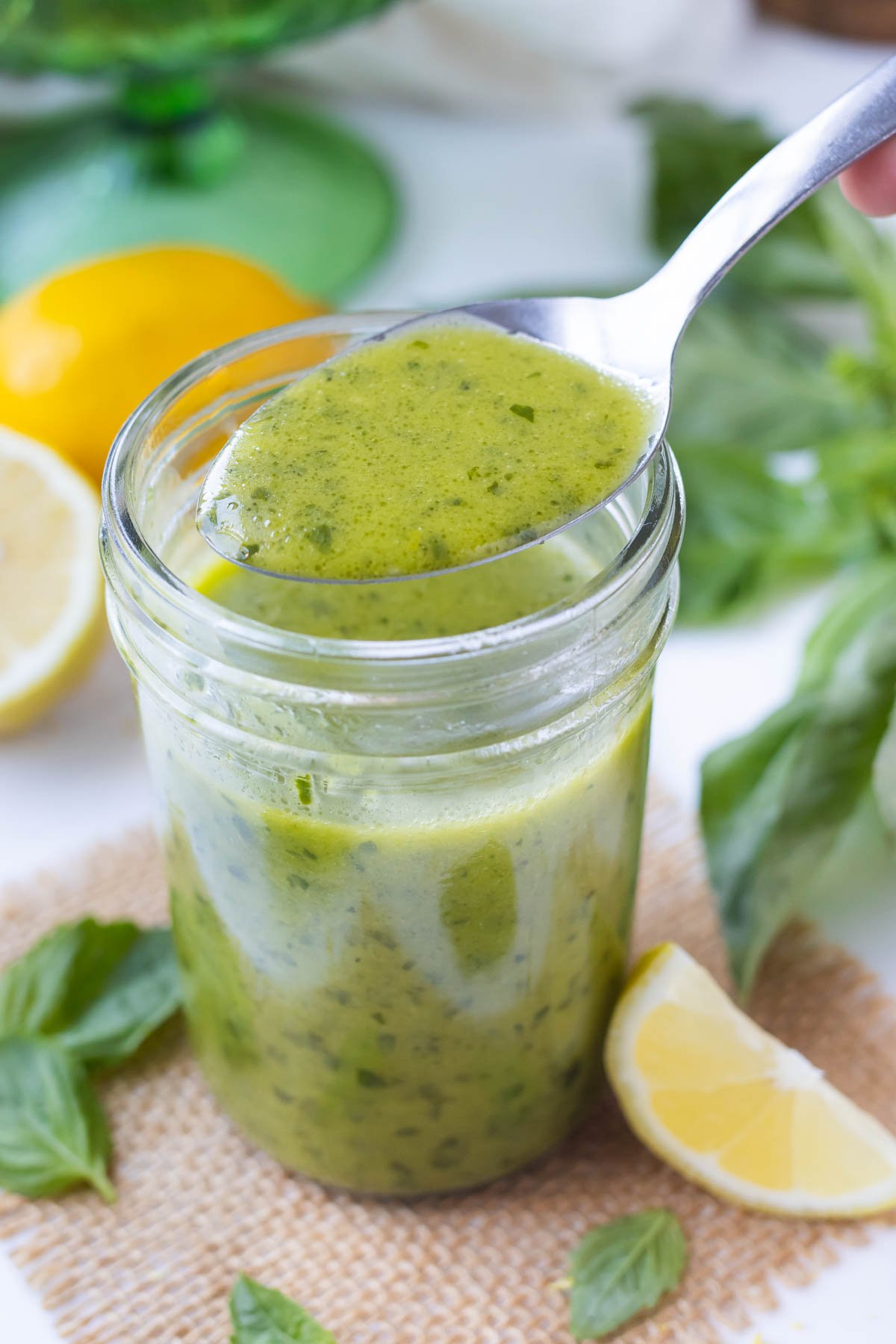 A spoon scoops some lemon basil vinaigrette dressing from a mason jar.