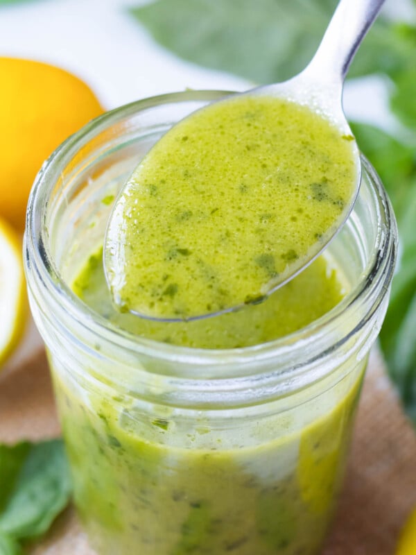 A spoon scoops up some lemon basil vinaigrette dressing from a glass mason jar.