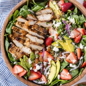 Grilled chicken is added on top of a spinach salad with strawberries and a balsamic vinaigrette.