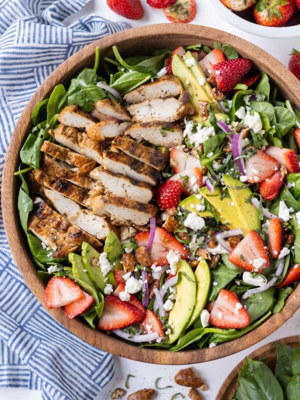 Grilled chicken is added on top of a spinach salad with strawberries and a balsamic vinaigrette.