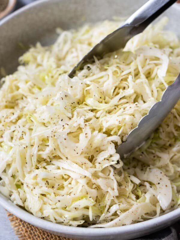 Tongs are used to stir and serve apple cider slaw.