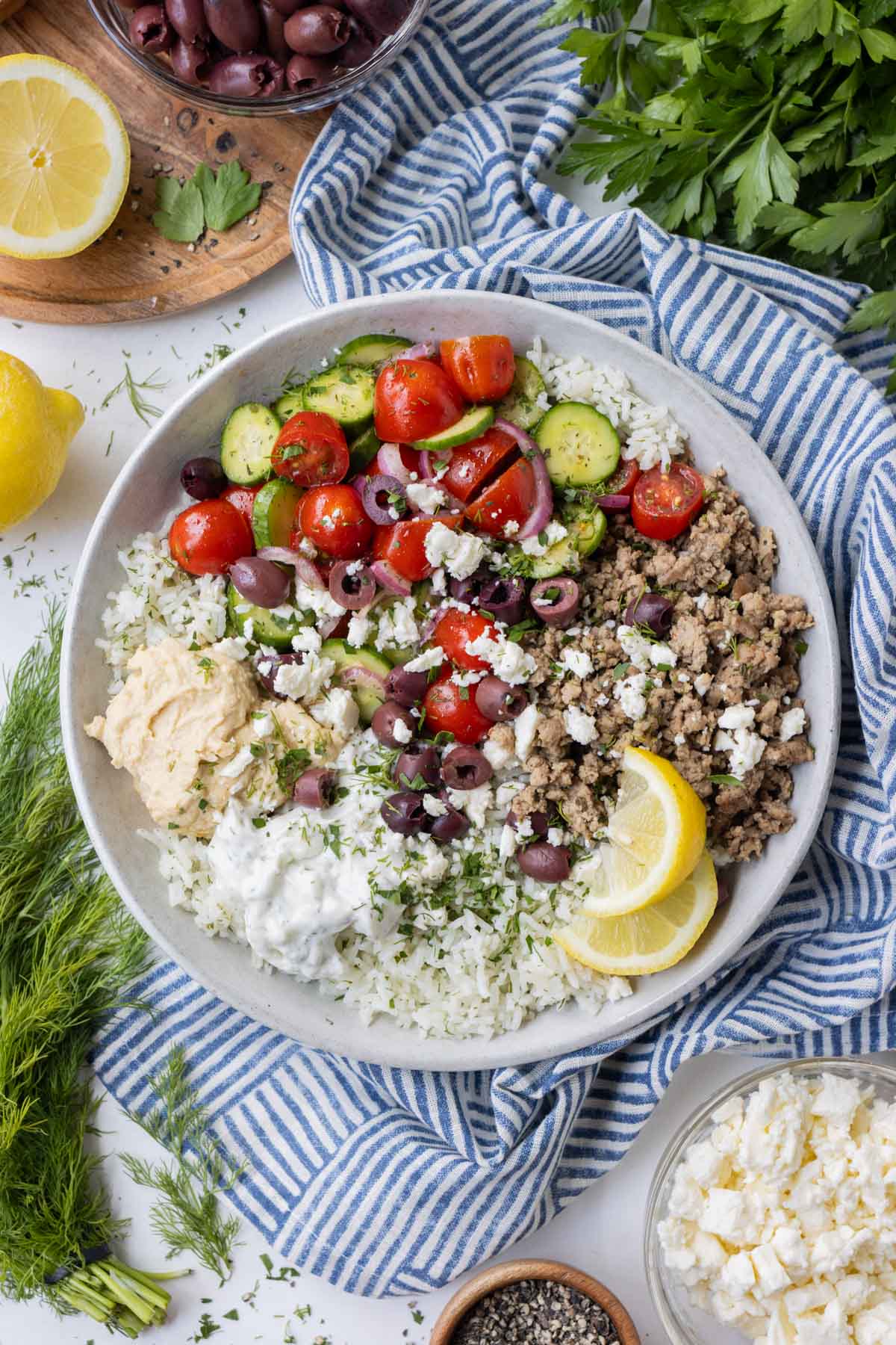 Greek turkey, cucumber-tomato salad, and other toppings are served on a bed of rice with a lemon wedge.