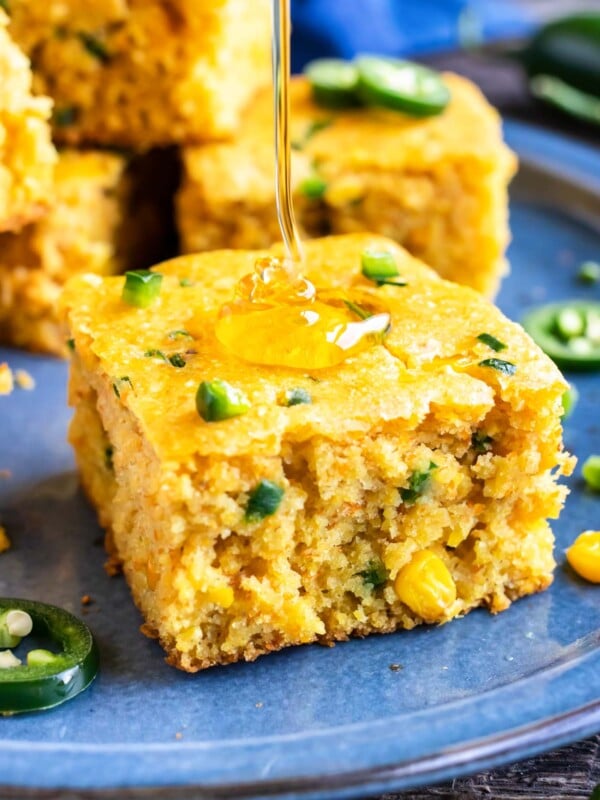 Extra honey is being drizzled on a slice of honey jalapeno cornbread on a blue plate.