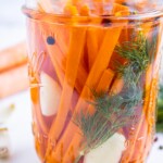 A mason jar is full of quick dill pickles carrots with garlic and pickling brine in a glass jar.