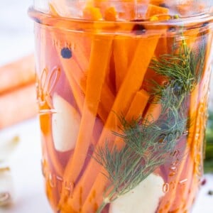 A mason jar is full of quick dill pickles carrots with garlic and pickling brine in a glass jar.