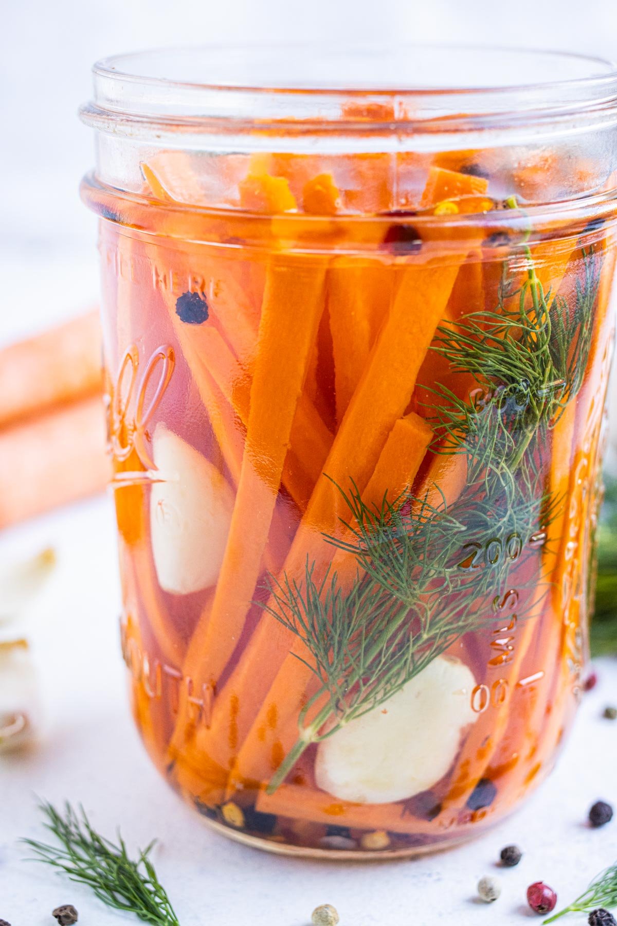 A mason jar is full of quick dill pickles carrots with garlic and pickling brine in a glass jar.