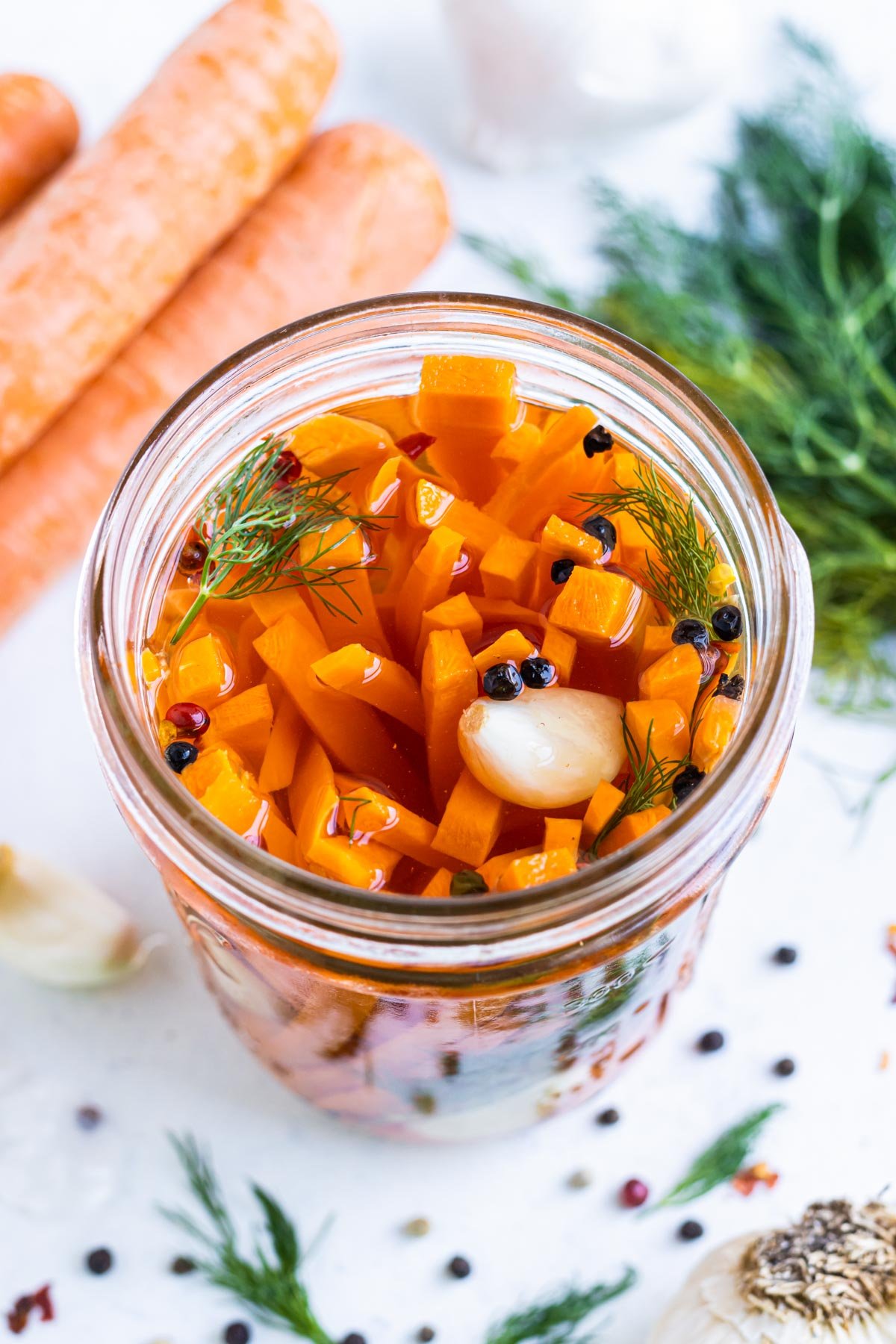 Quick pickled carrots and dill are in a jar with a pickling solution.