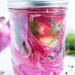 Quick pickled red onions with fresh dill is in a mason jar with garlic and peppercorns.