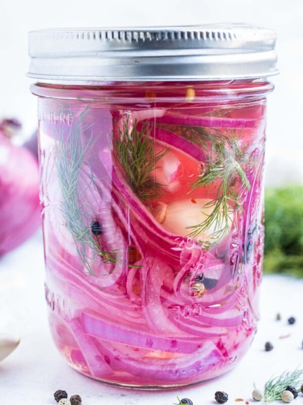 Quick pickled red onions with fresh dill is in a mason jar with garlic and peppercorns.