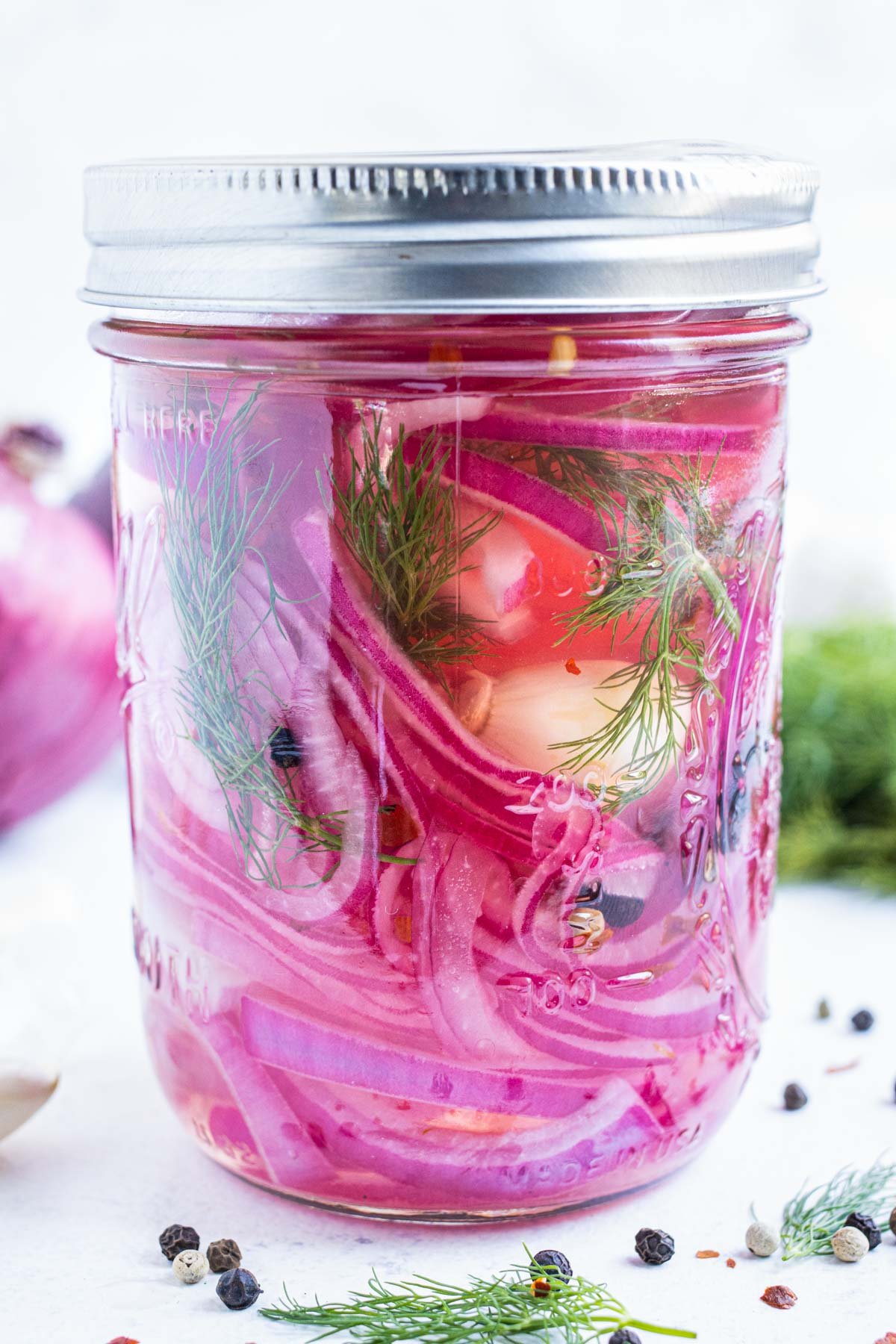 Quick pickled red onions with fresh dill is in a mason jar with garlic and peppercorns.