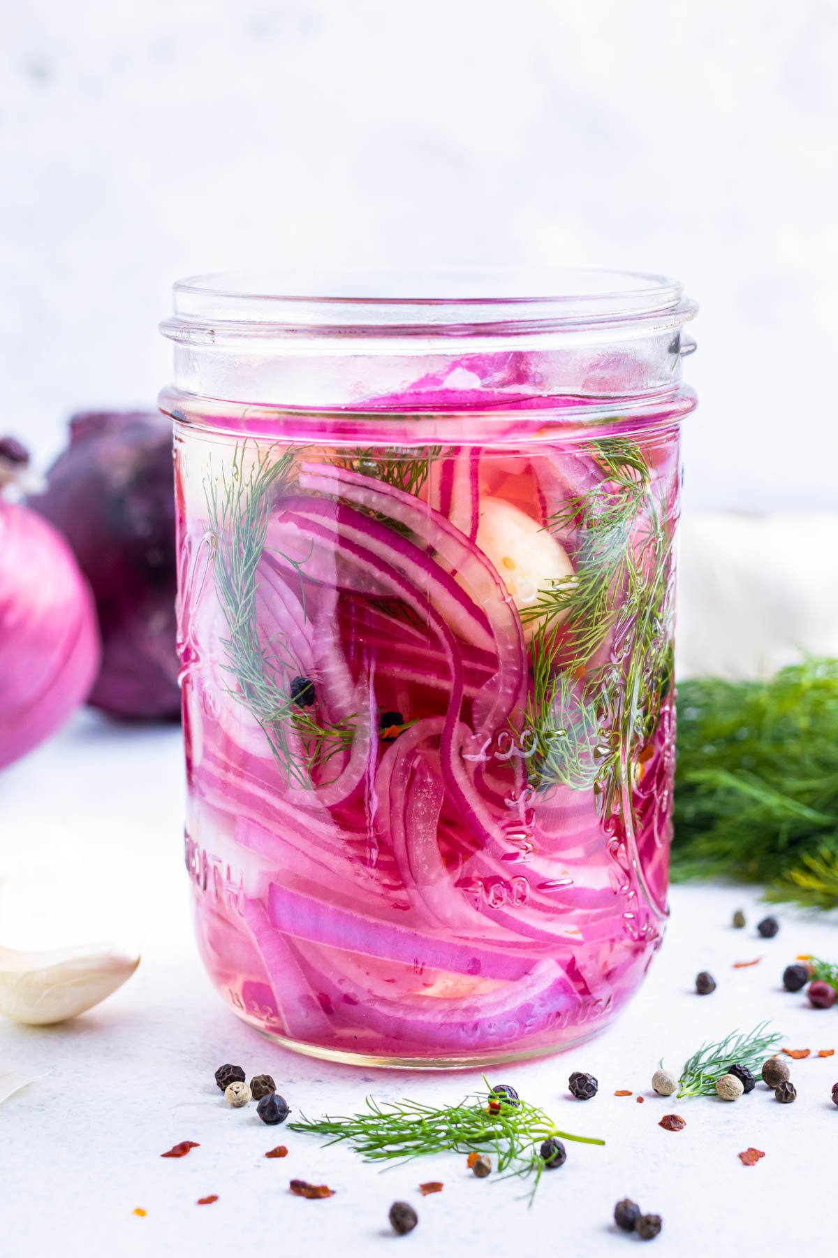 A jar of quick pickled red onions is filled with garlic, dill and a brining solution.