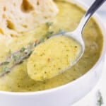 A metal spoon lifts homemade zucchini soup from a bowl.