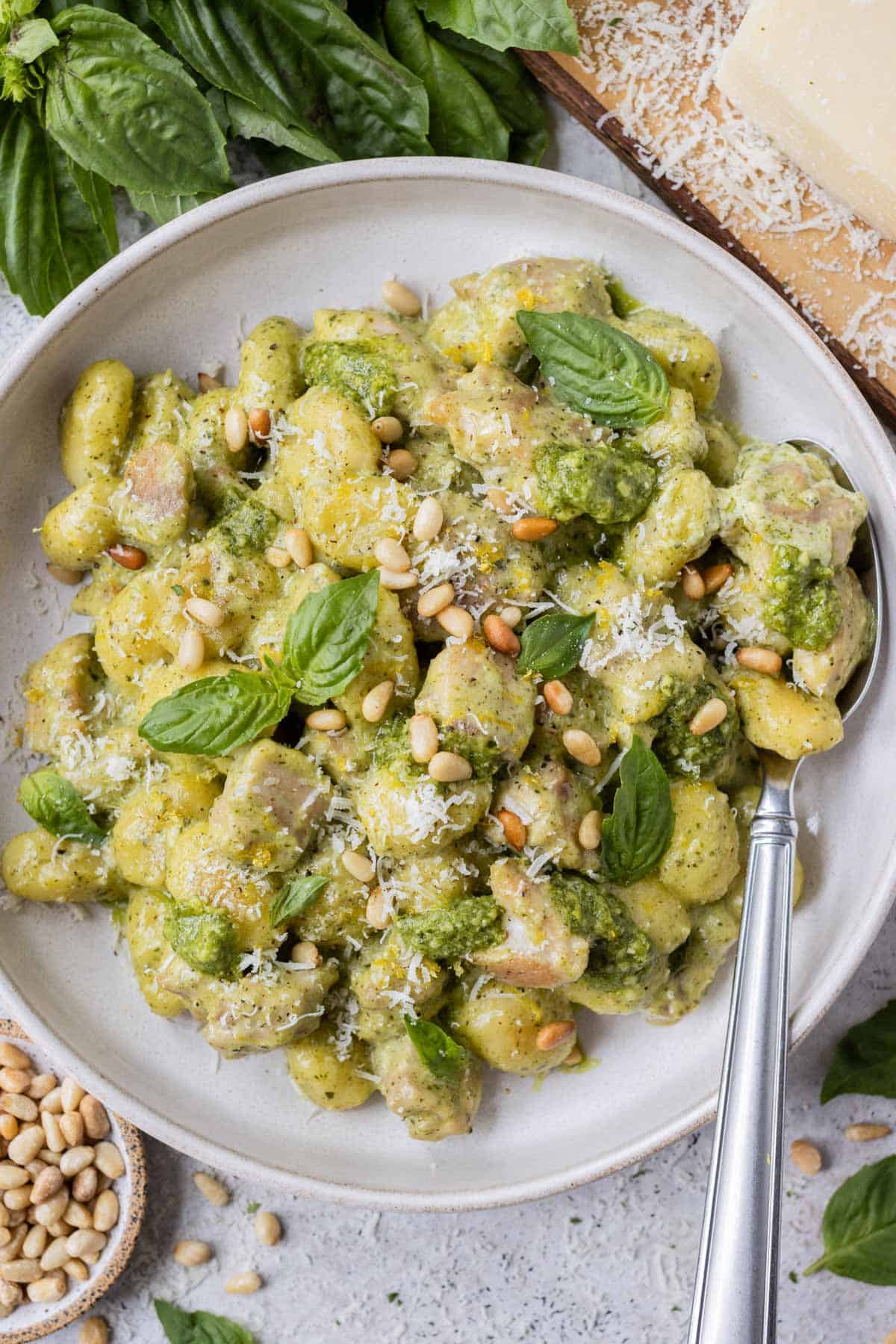 A white bowl is full of chicken and gnocchi in a creamy pesto sauce.