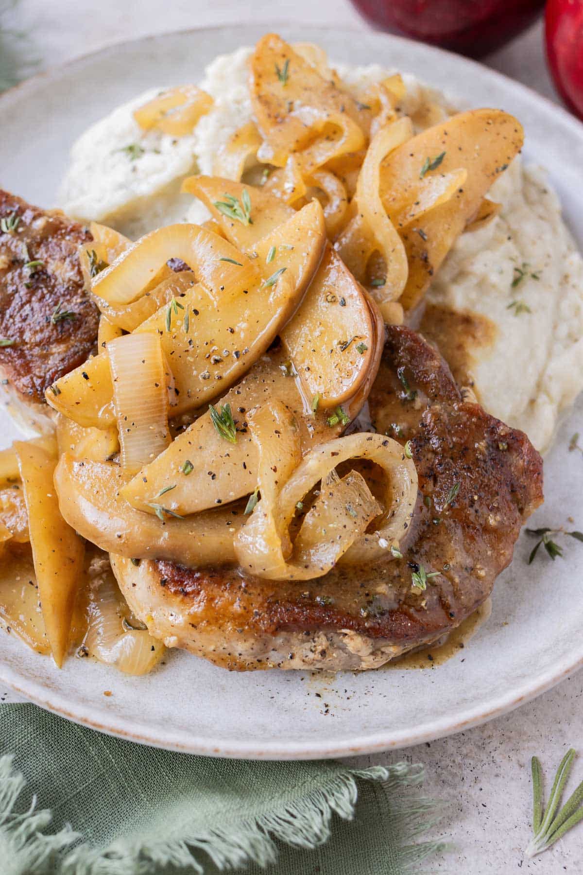 Bone in pork chops, apples, and onions are served on a white plate with mashed potatoes.