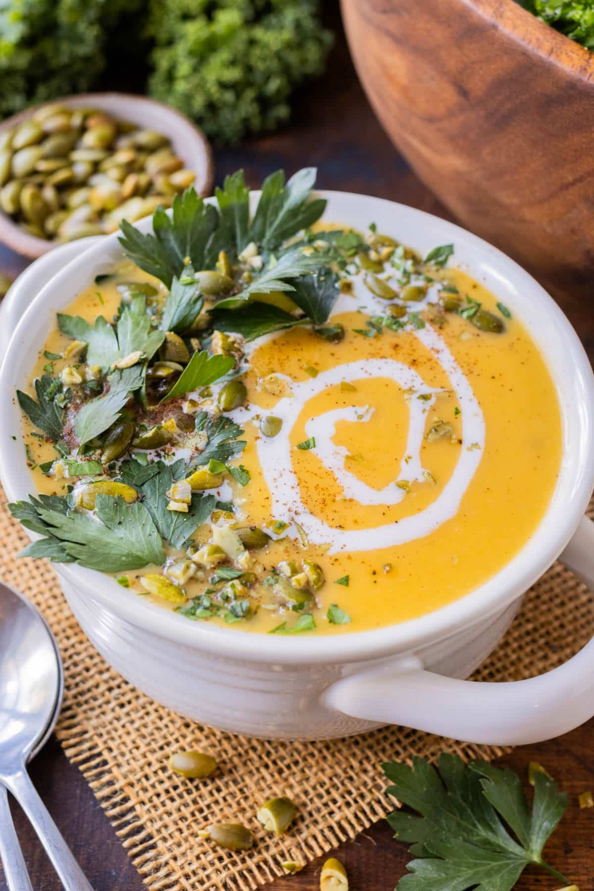 A white bowl is full of a creamy roasted butternut squash soup made with coconut milk and served with pumpkin seeds.