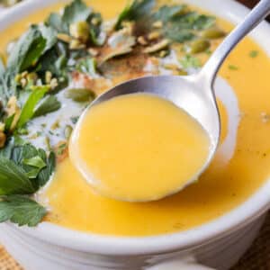 A spoon scoops up some creamy roasted butternut squash soup from a white bowl.