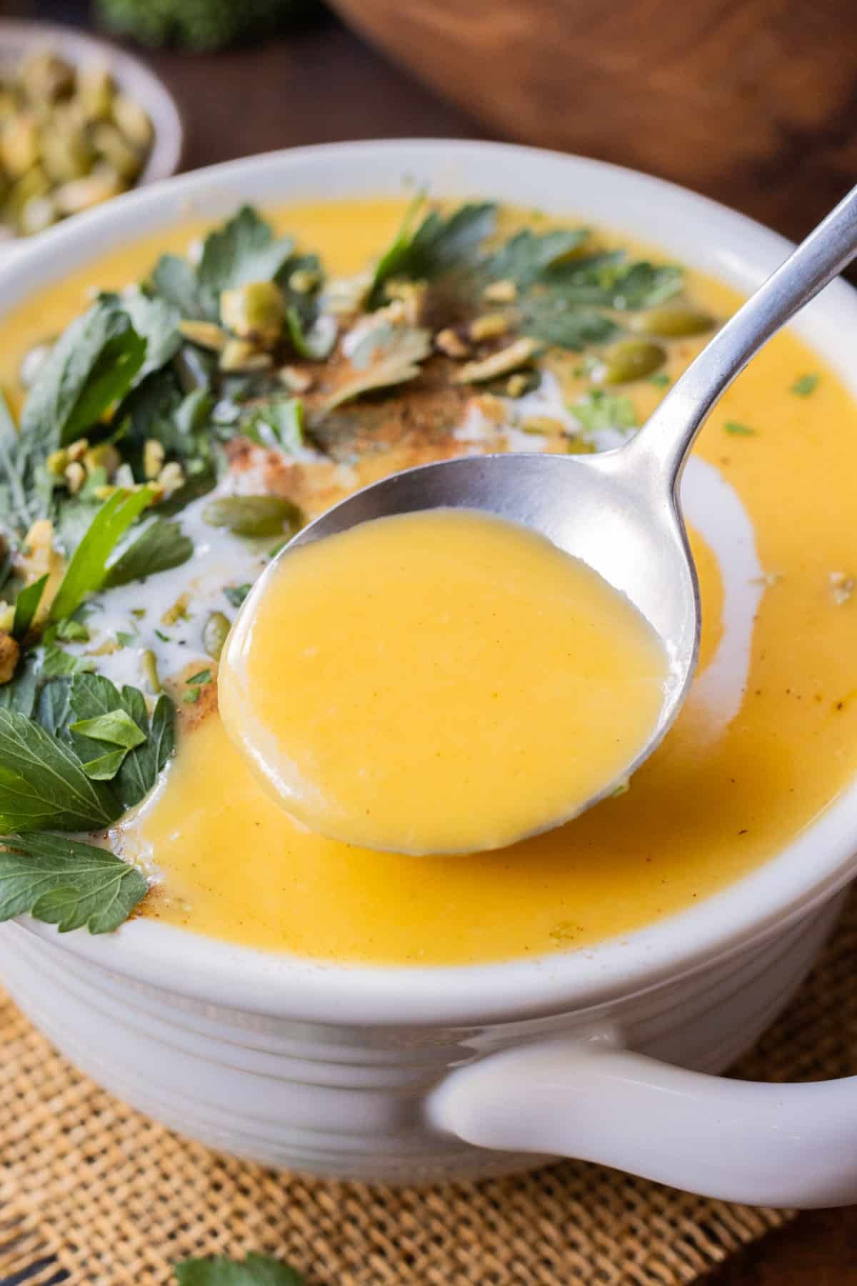 A spoon scoops up some creamy roasted butternut squash soup from a white bowl.
