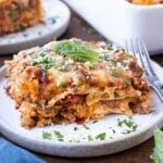 A piece of an easy lasagna recipe is on a white plate with a fork next to it and parsley sprinkled around.