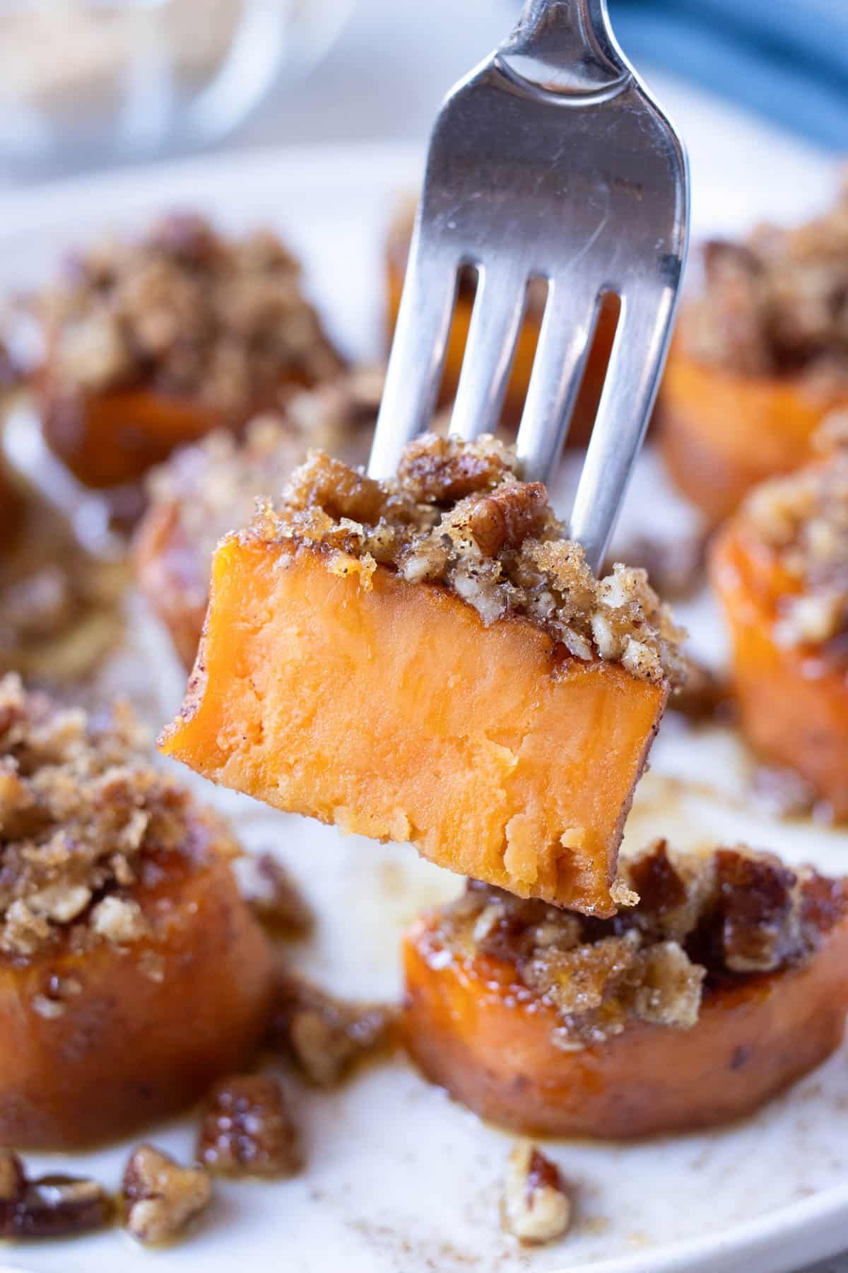 A fork picks up a bite of melting sweet potatoes with a pecan topping.