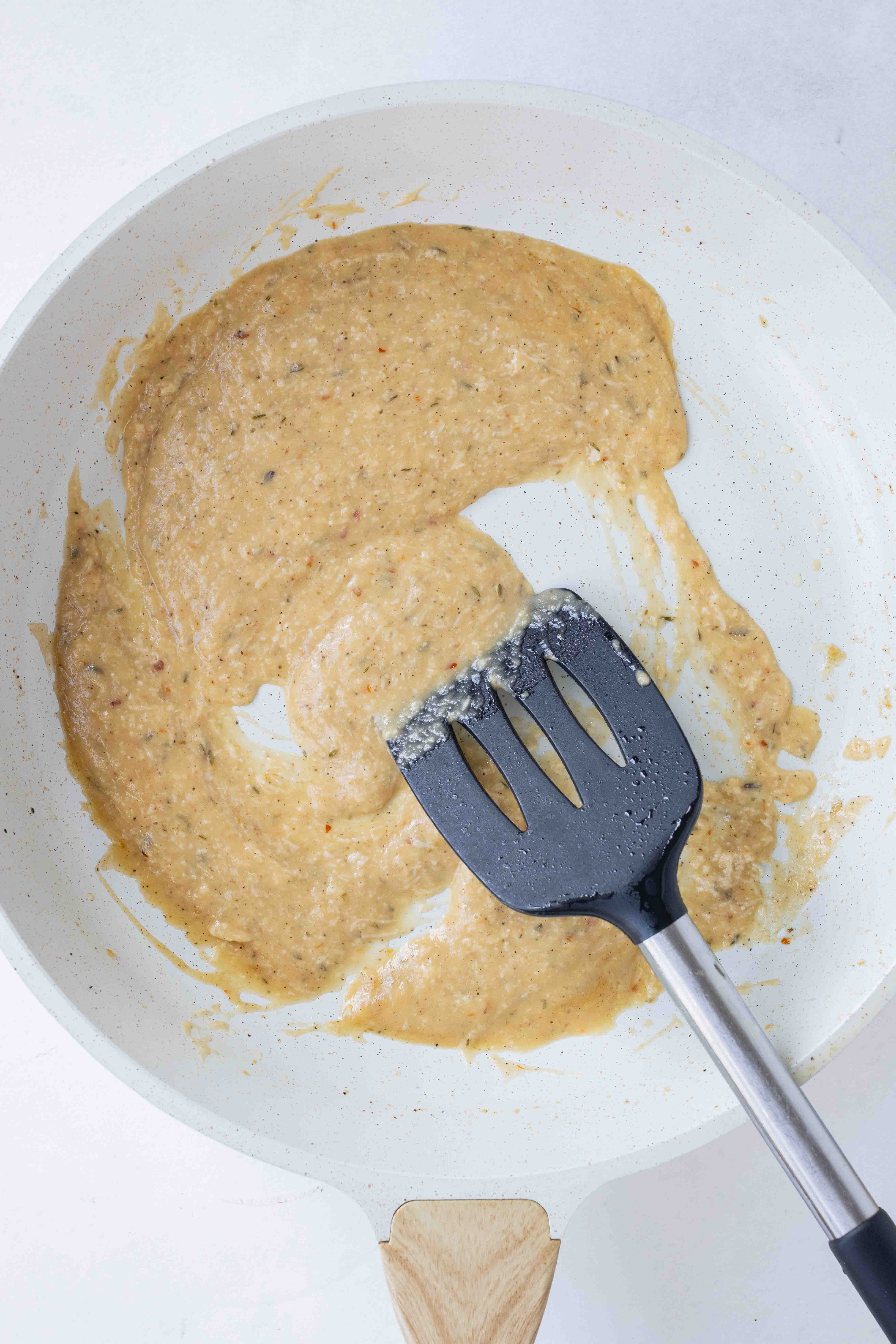 Creamy mushroom pappardelle sauce is stirred in a skillet with a spatula.