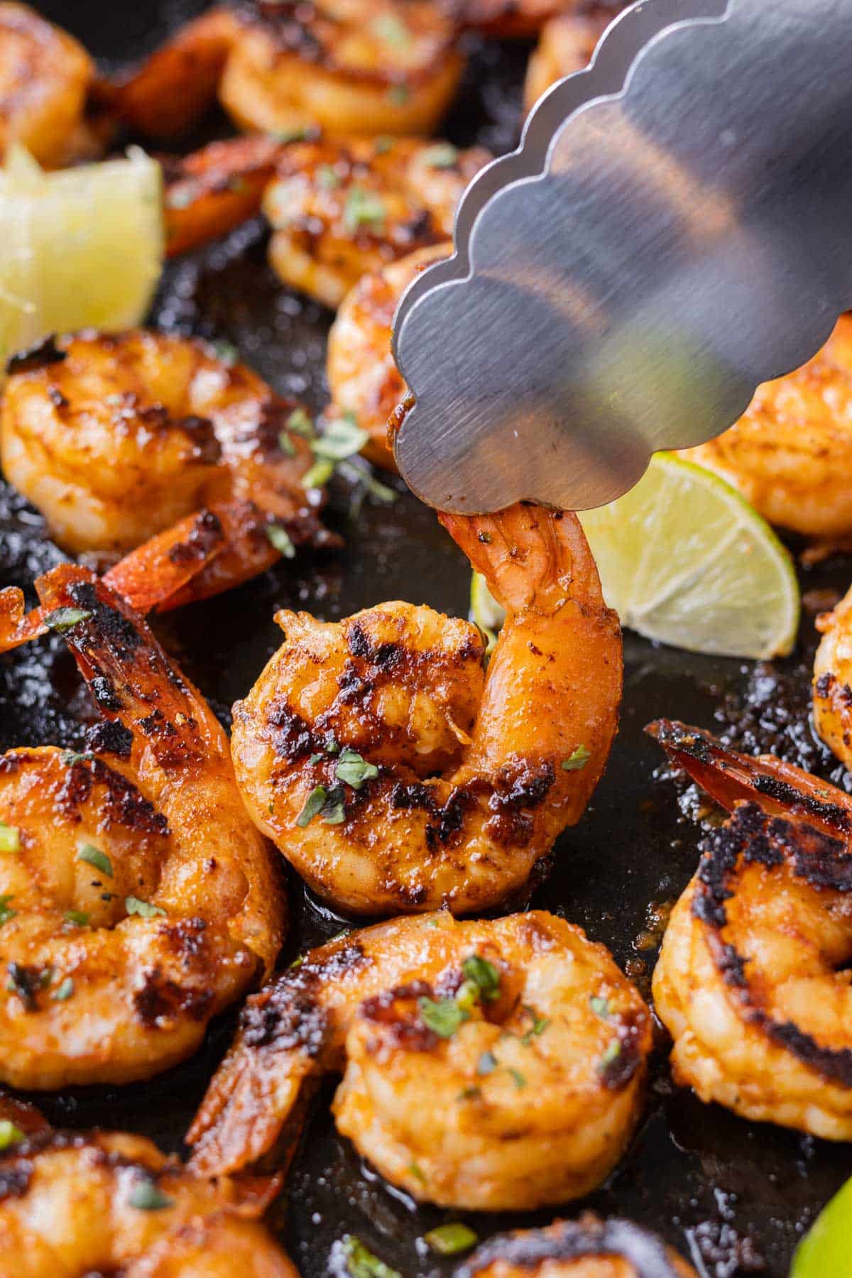 Shrimp are cooked in a skillet in a chili garlic lime sauce with lime wedges.