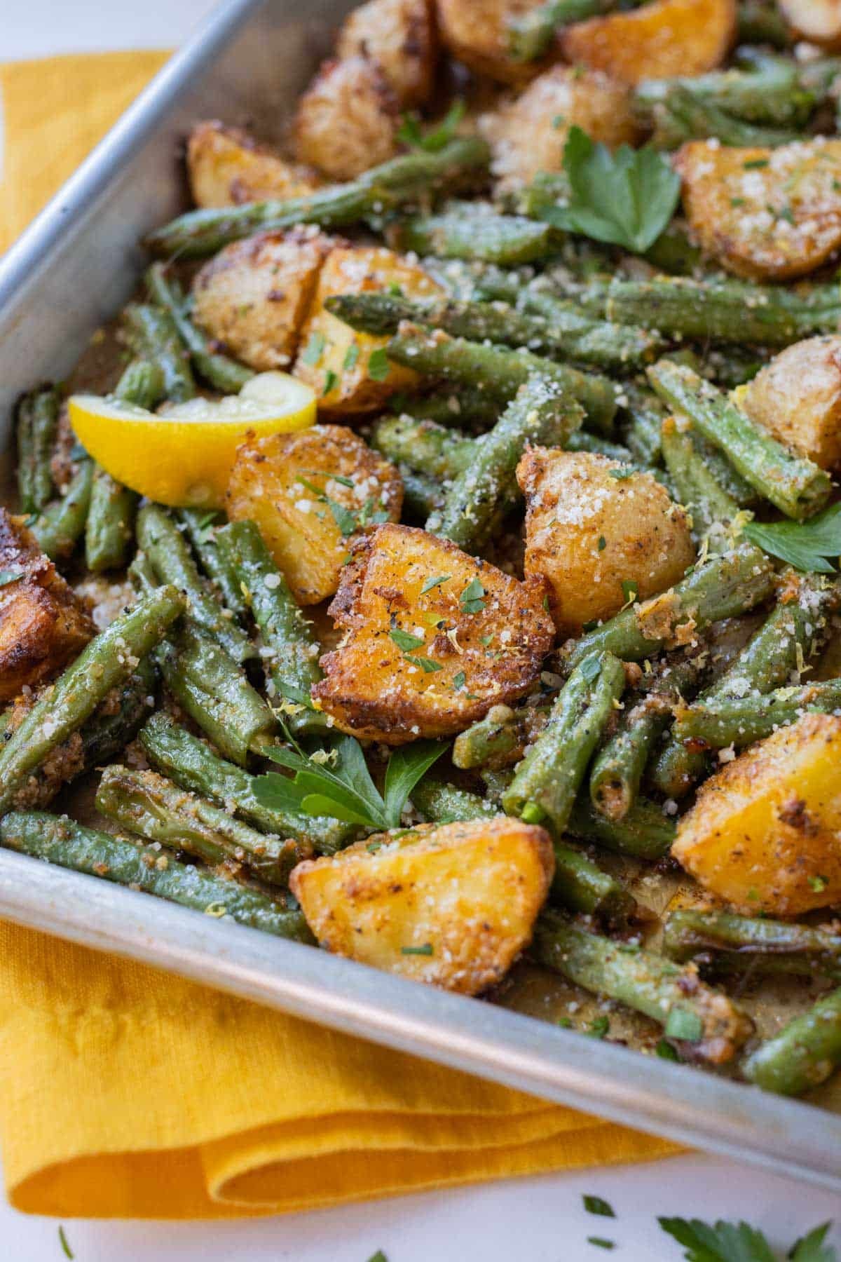 Potatoes and green beans are roasted on a baking sheet for an easy side dish.