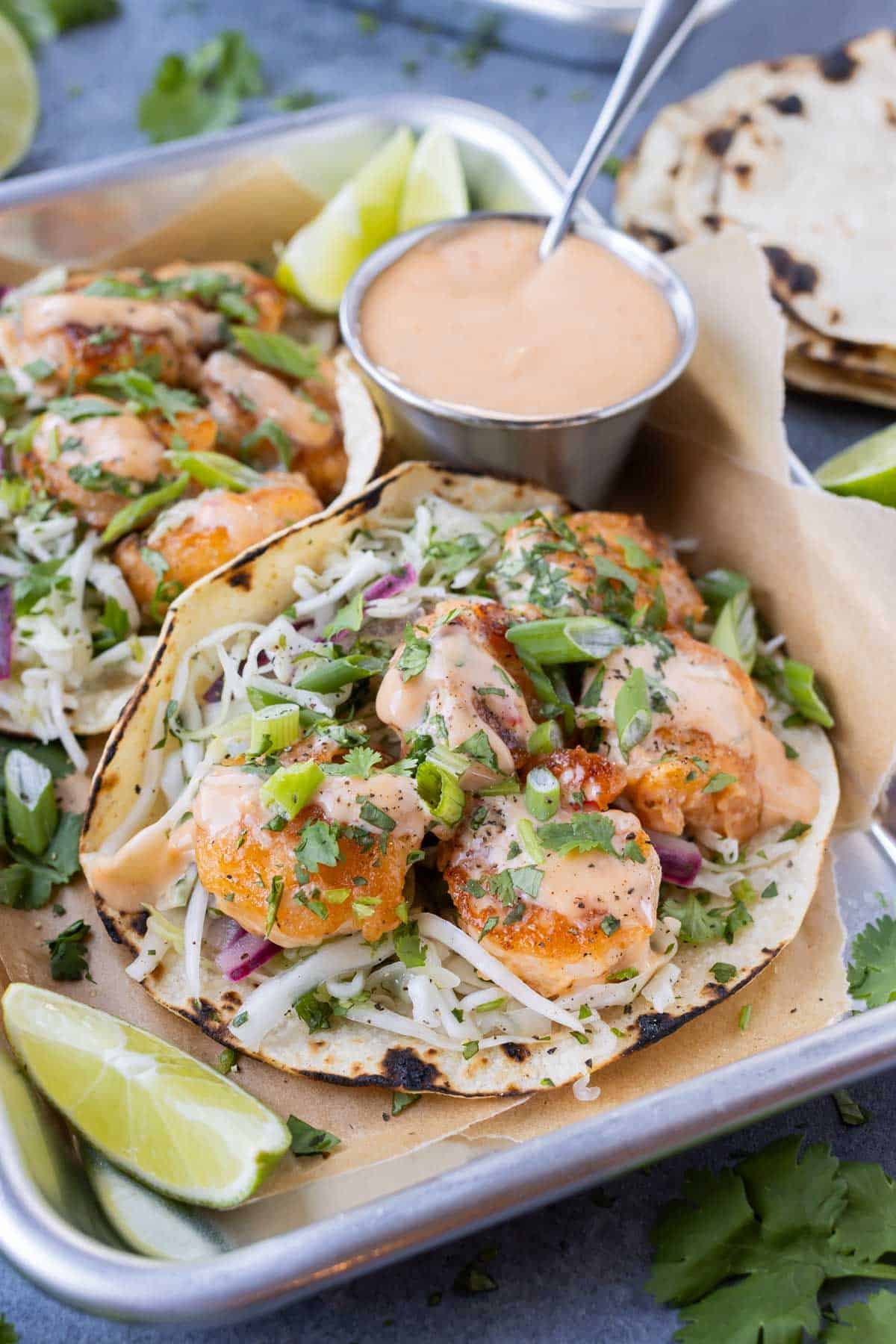 Extra Bang Bang sauce is served with shrimp tacos on a tray.